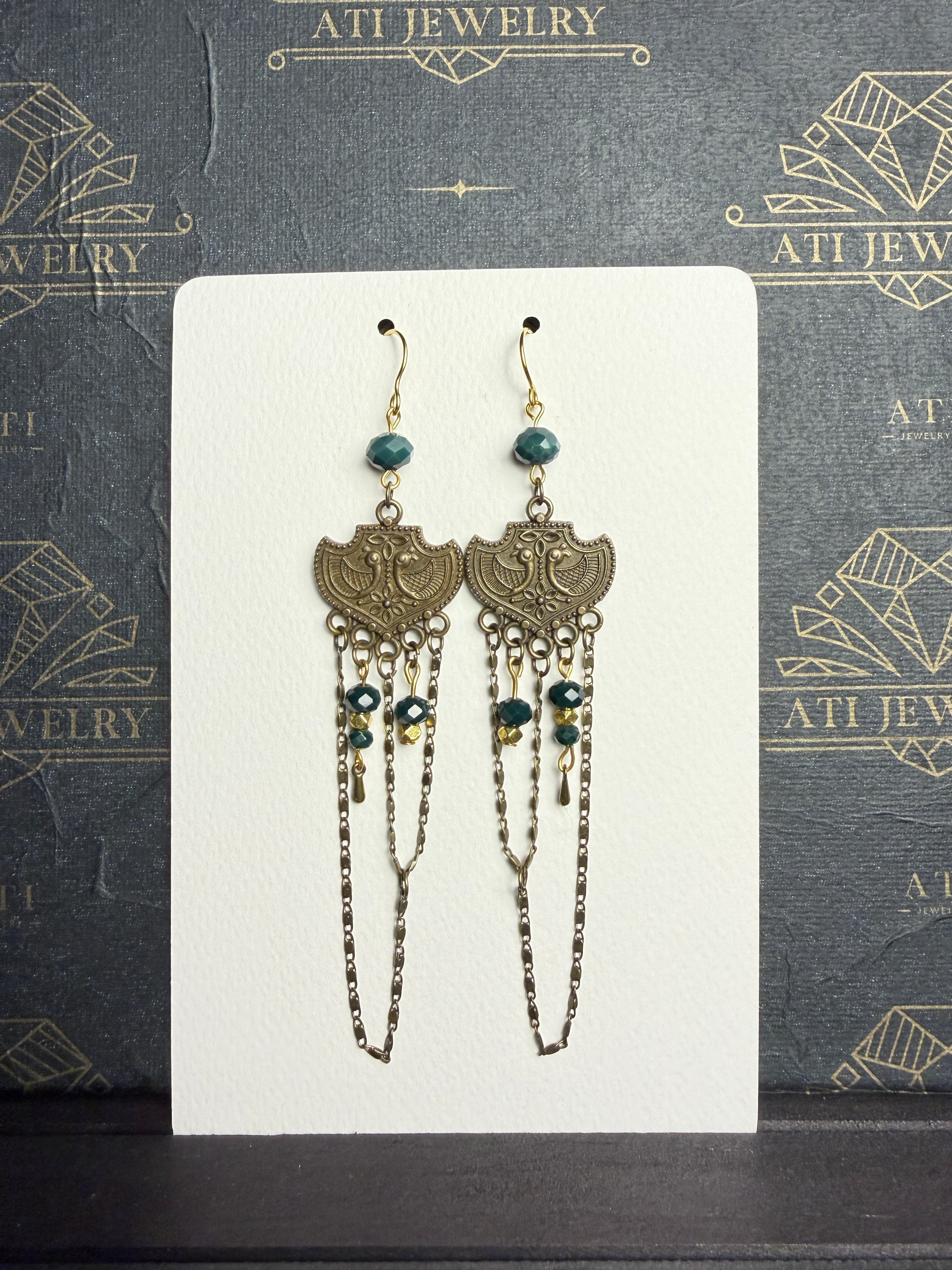 Long chandelier earrings with teal and golden-yellow beads, antique brass-tone bird plaques, and layered chain loops on a cream display card.