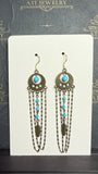 Long chandelier earrings with turquoise beads, antique brass-tone circular ornaments, feather charms, and layered chain loops on a cream display card.