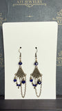 Antique brass-tone chandelier earrings with royal blue faceted beads, floral fan-shaped panels, dangling accents, and draped chains.