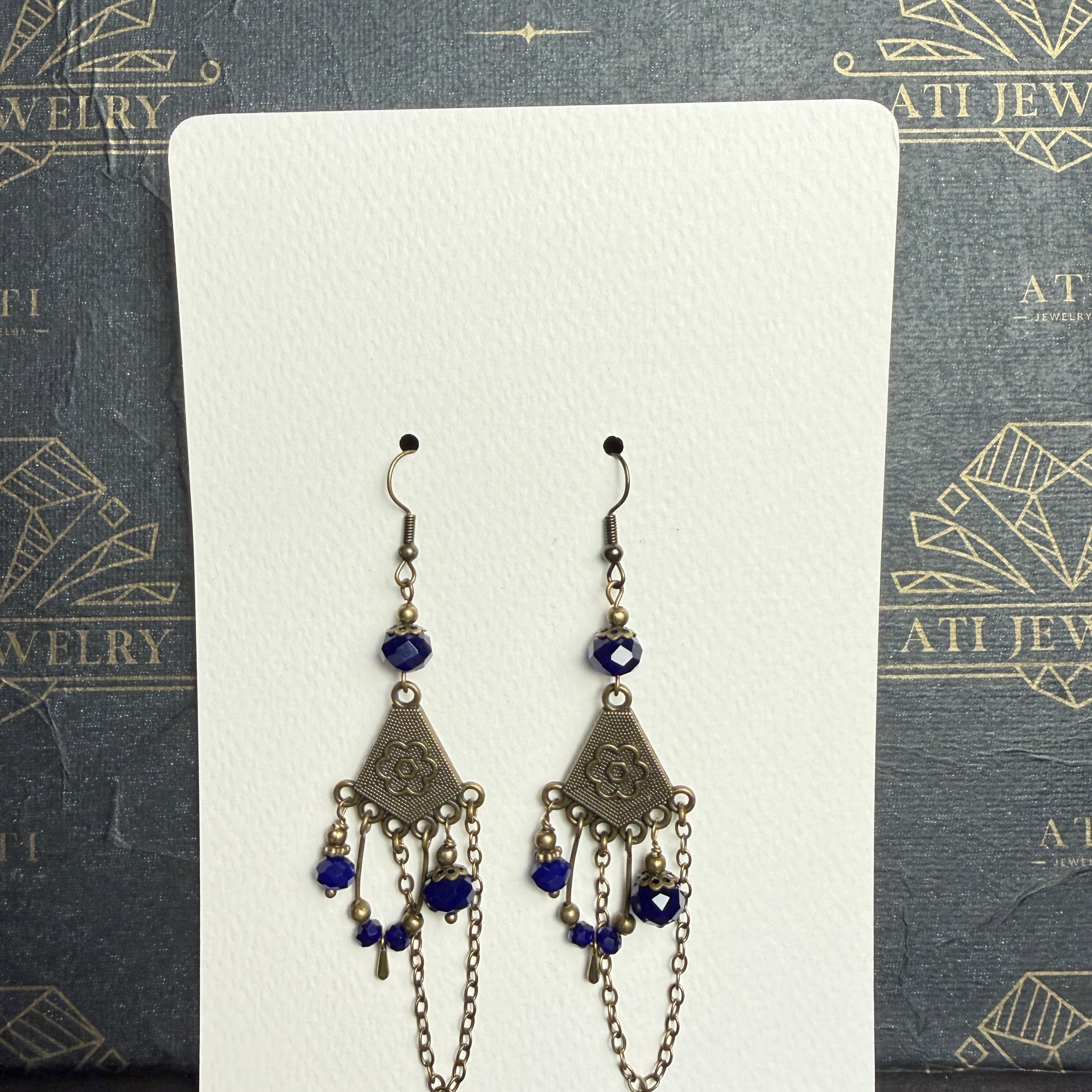 Antique brass-tone chandelier earrings with royal blue faceted beads, floral fan-shaped panels, dangling accents, and draped chains.
