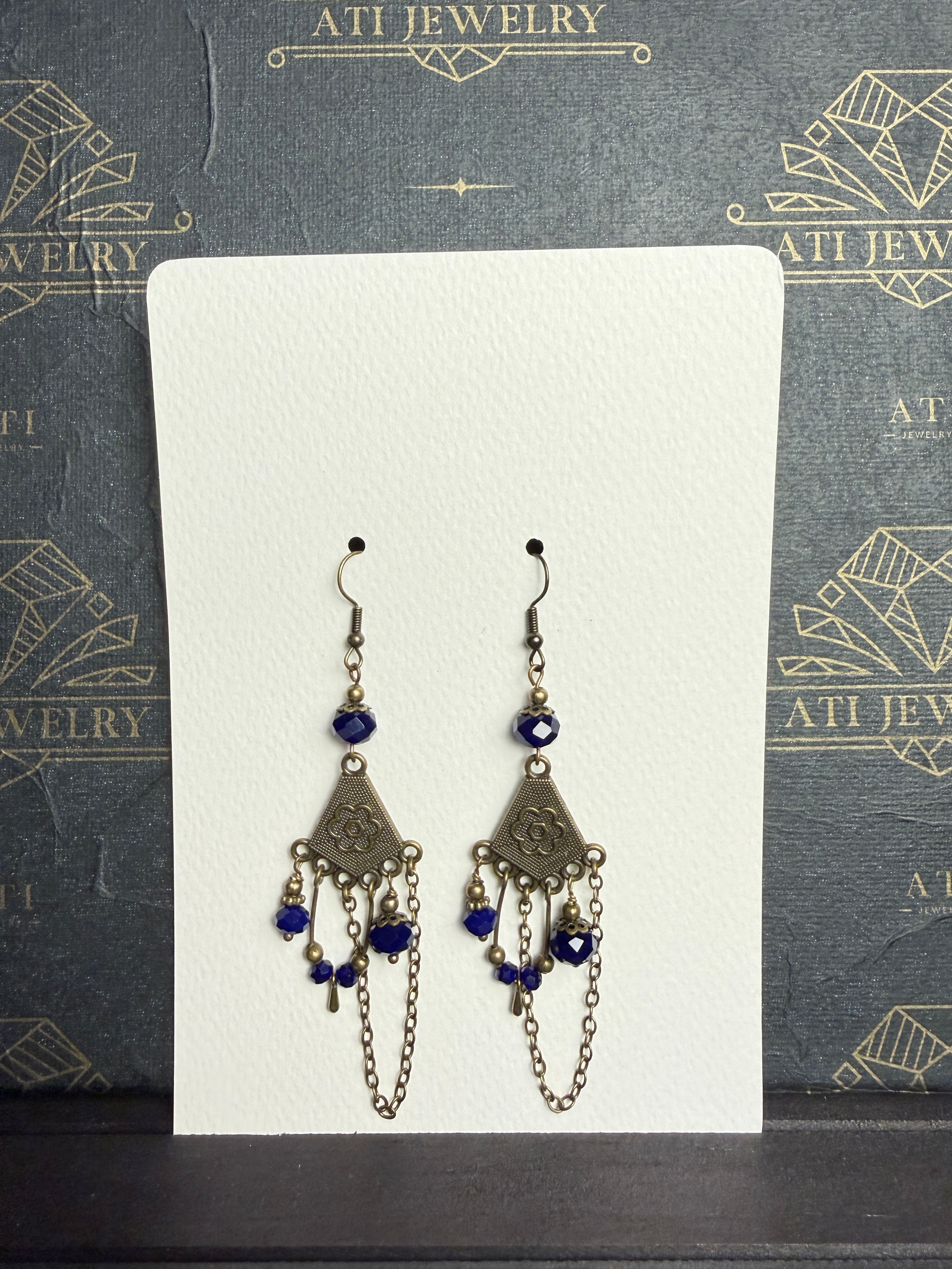 Antique brass-tone chandelier earrings with royal blue faceted beads, floral fan-shaped panels, dangling accents, and draped chains.