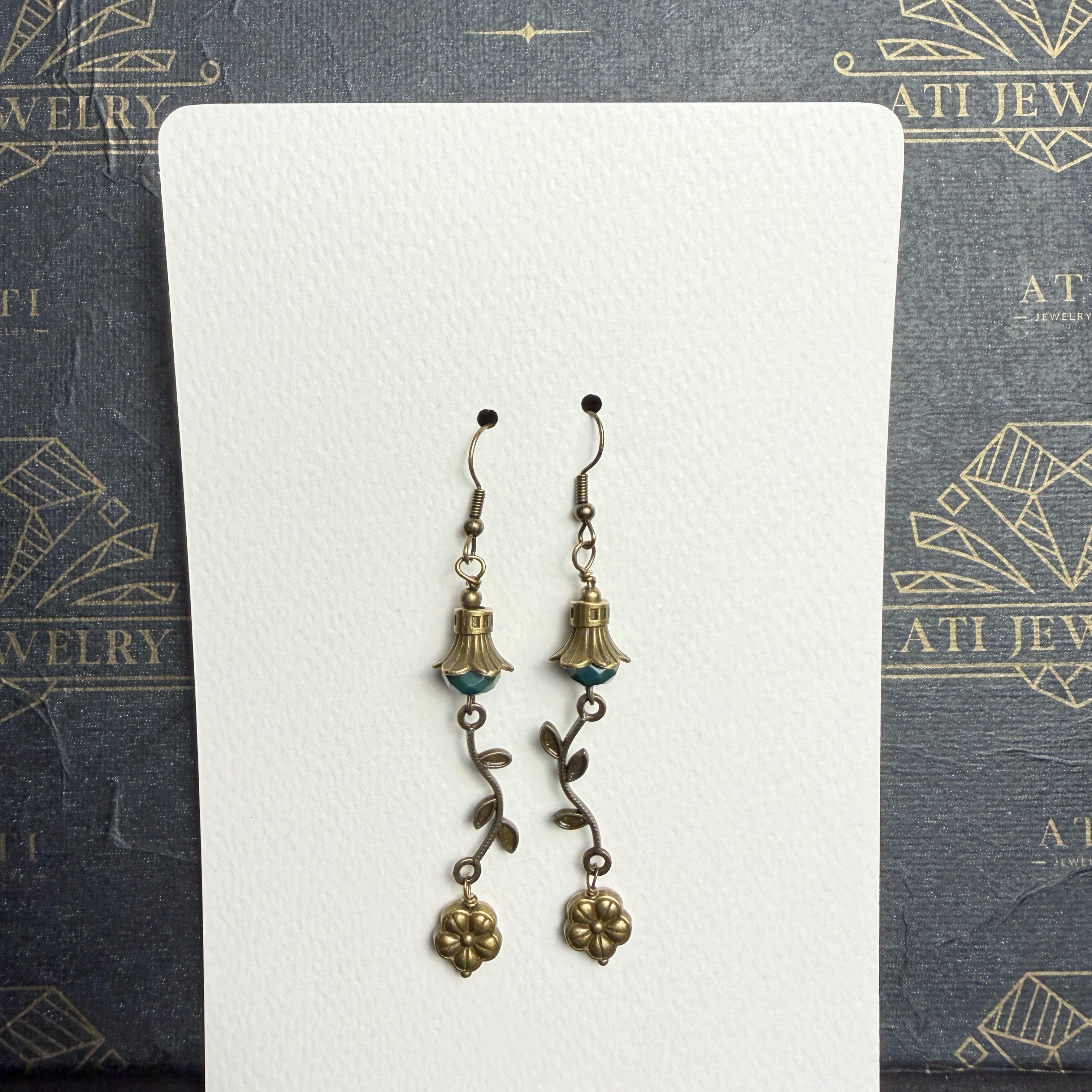 Antique brass-tone drop earrings with faceted teal beads, petal-shaped caps, curved leafy vines, and dangling flower charms.