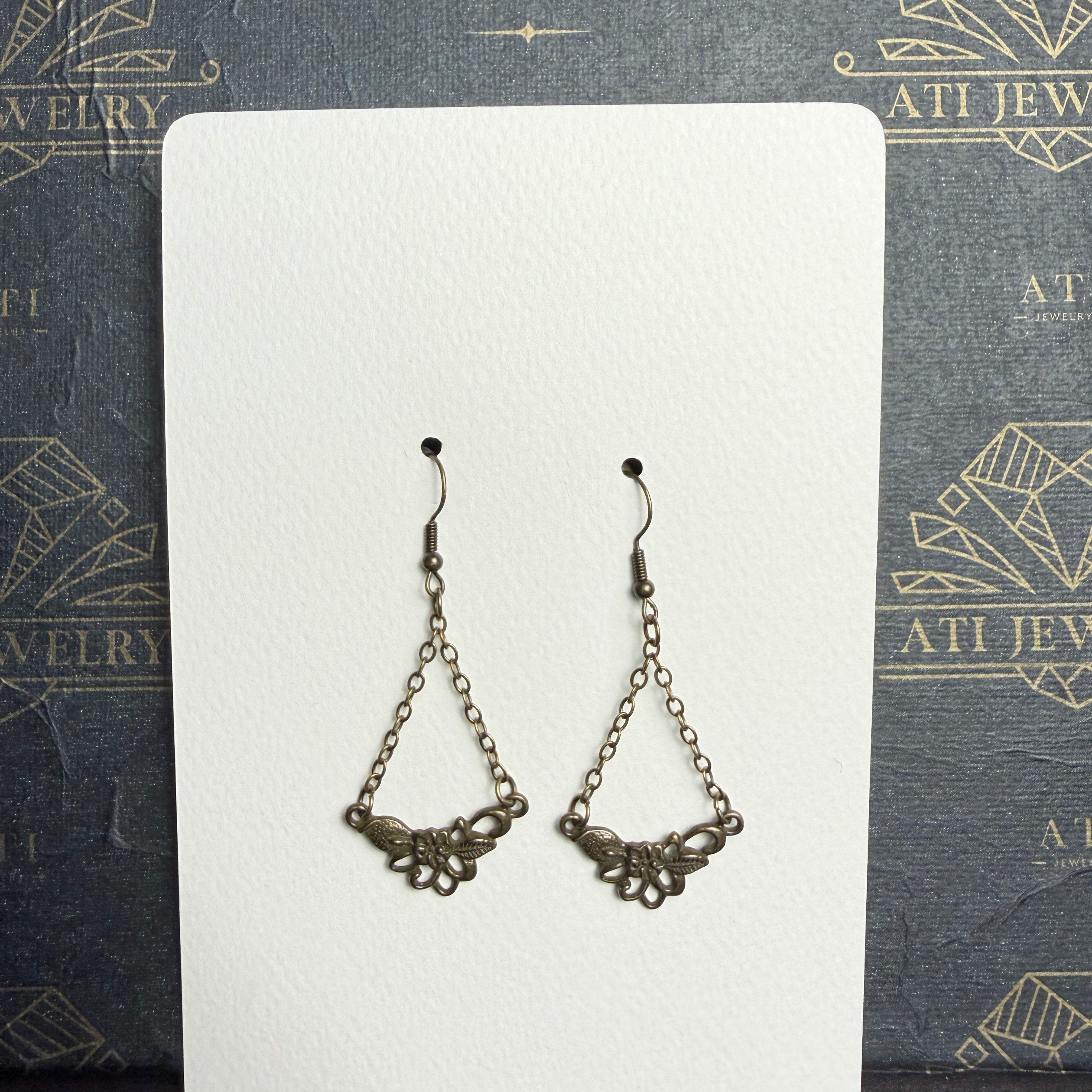 Antique brass-tone chain drop earrings with open floral and textured leaf details, displayed on an ATI JEWELRY Vintage Collection card.