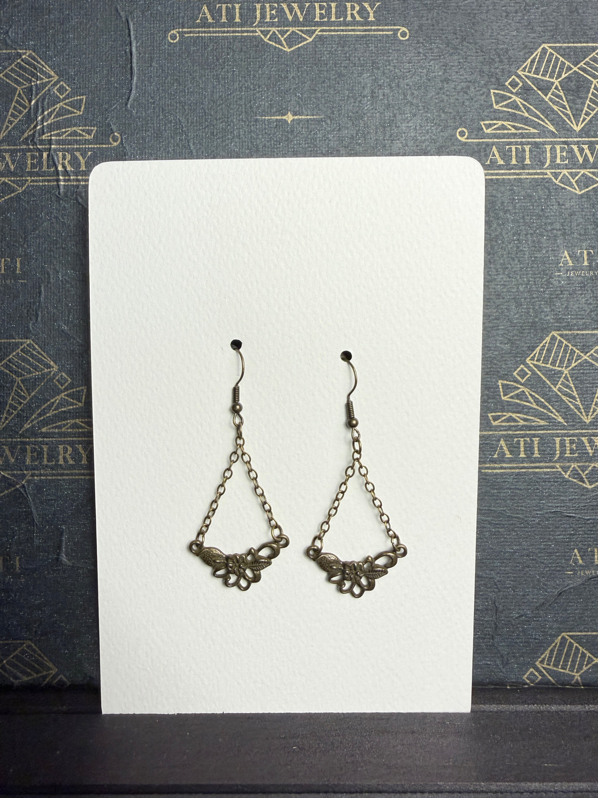 Antique brass-tone chain drop earrings with open floral and textured leaf details, displayed on an ATI JEWELRY Vintage Collection card.